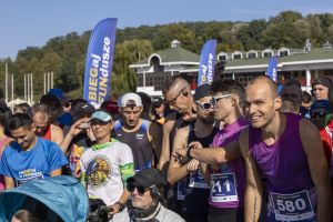 Tuż przed startem: biegacze w kolorowych koszulkach, w tym zawodnik w fiolecie sprawdza zegarek sportowy.