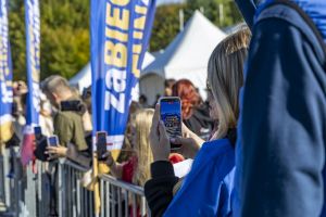 Kibice za barierką filmują telefonami start biegu; na ekranie widać tłum pod niebieską bramą zaBIEGaj o FUNdusze.