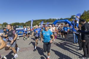 Biegacze na bruku w słońcu; na czele mężczyzna w koszulce Poznań Maraton w czerwonych okularach.