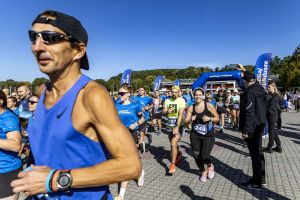 Uśmiechnięci biegacze z numerami 249 i 107 w zielonej koszulce Night Runners mijają kamerę przy bramie startowej.