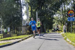 Biegacz w niebieskiej bluzie z numerem 623 obok zawodnika w fluo-żółtym singlecie na moście nad Cybiną.