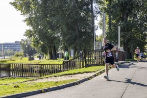 Biegacz w okularach z numerem 37 trzyma niebieską butelkę podczas biegu aleją z widokiem na jezioro.