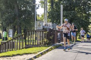 Uśmiechnięty uczestnik z numerem 11 unosi oba kciuki w górę w biegu między drzewami.