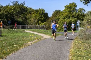 Uczestnicy z numerami 181 i 81 na zakręcie trasy; mężczyzna w niebieskim stroju sprawdza zegarek sportowy.