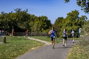 Grupa biegaczy na krętej parkowej alei; na pierwszym planie mężczyzna w niebieskim bezrękawniku i kobieta z numerem 81.