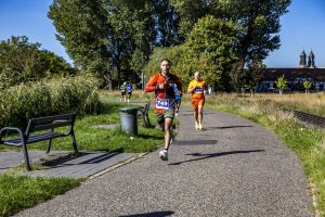 Biegacz w pomarańczowo-czarnej koszulce z numerem 749 na ścieżce obok torów; w tle wieże katedry poznańskiej.