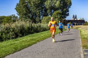Łysy biegacz w pomarańczowym stroju z numerem 299 na pierwszym planie; za nim uczestnicy w niebieskich koszulkach.