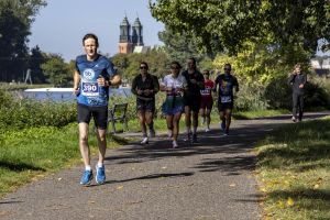 Biegacz z numerem 390 na pierwszym planie w towarzystwie kilkunastu uczestników na jesiennej alei nad Maltą.