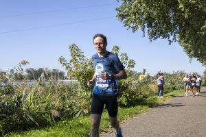 Biegacz z numerem 390 w koszulce Biegające Luboń na ścieżce między trzcinami a drzewami nad Maltą.