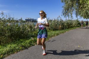 Uśmiechnięta biegaczka w koszulce Run Team z tęczową spódnicą biegnie w stronę obiektywu w słoneczne popołudnie.