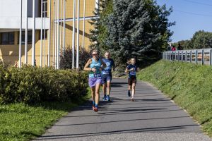 Trójka biegaczy z numerami 399, 246 i 412; po lewej żółty budynek z kolumnami i wysoki świerk.