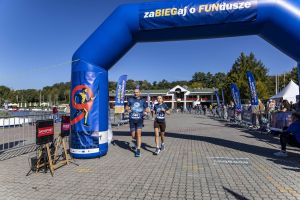 Para z numerami 246 i 412 wbiega pod niebieską dmuchaną bramę z napisem zaBIEGaj o FUNdusze; obok ekrany DATASPORT.