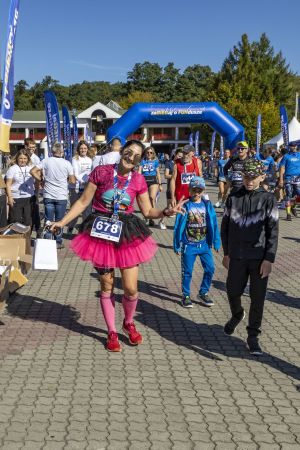 Uczestniczka w różowej koszulce, tutu i różowych skarpetach z numerem 678 z medalem i torbą pod bramą finiszową.