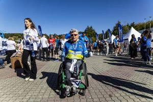 Uczestnik na wózku sportowym w koszulce Michelin z medalem pokazuje oba kciuki w tłumie przy niebieskiej bramie.
