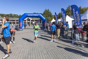 Kobieta w limonkowej koszulce z numerem 473 biegnie w stronę niebieskiej bramy finiszowej; za barierkami kibice.