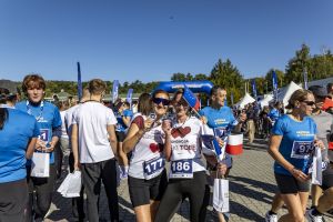 Partnerki biegu z numerami 177 i 186 pozują z medalami i małymi flagami na tle niebieskiej bramy i namiotów.