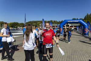 Uśmiechnięty mężczyzna z numerem 544 w czerwonej koszulce Drużyna Szpiku z medalem przy bramie finiszowej.