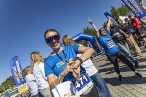 Biegaczka z numerem 471 sprawdza zegarek sportowy, obok uczestniczka z numerem 333 świętuje z uniesionymi rękami.