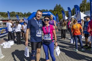 Mężczyzna z numerem 685 i partnerka z numerem 705 obejmują się z medalami przy niebieskiej bramie mety.
