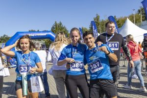 Młoda para z numerami 380 i 387 pokazuje medale w tłumie finisherów przy dmuchanej bramie biegu.