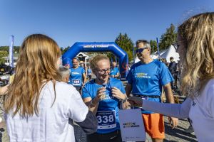Wolontariuszka wręcza biegaczce z numerem 338 medal i papierową torbę z logo zaBIEGaj o FUNdusze.