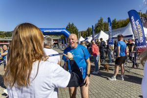 Wolontariuszka zakłada medal finishera uczestnikowi w niebieskiej koszulce biegamy.org przy bramie mety.
