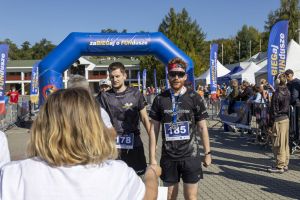 Dwaj biegacze Runmaggedon z numerami 185 i 178 z medalami stoją pod niebieską bramą zaBIEGaj o FUNdusze.