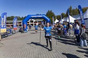 Uśmiechnięta uczestniczka nordic walking z numerem 182 idzie pod niebieską bramą zaBIEGaj o FUNdusze na Malcie.