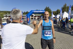 Zadowolony biegacz z numerem 734 wymienia uścisk przedramion z osobą witającą go przy mecie biegu.