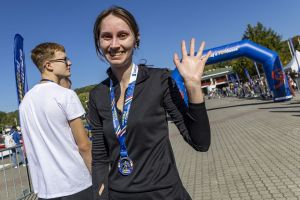 Biegaczka z medalem finishera na wstążce macha ręką na tle dmuchanej bramy mety zaBIEGaj o FUNdusze.