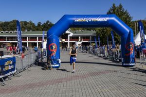 Mężczyzna z numerem 377 w czapce biegnie pod bramą i sprawdza czas na zegarku sportowym.