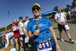 Biegaczka w limonkowej czapce z numerem 411 unosi medal po ukończeniu trasy w słoneczny dzień.