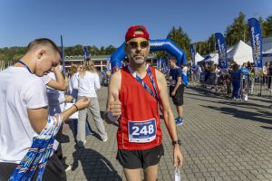 Biegacz w czerwonej koszulce z numerem 248 z medalem pokazuje kciuk w górę przy bramie mety.