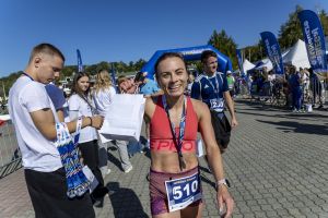 Radosna biegaczka z numerem 510 unosi białą torbę upominkową w tłumie uczestników przy mecie.