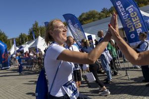 Blondynka w okularach z numerem 206 przybija piątkę w strefie kibiców między niebieskimi flagami biegu.