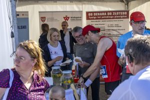 Biegacz z numerem 48 sięga po przekąskę przy stoisku z banerem o historii polskiego pieniądza.
