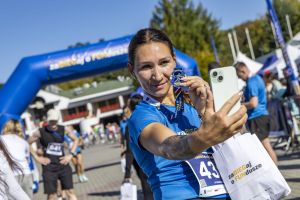 Biegaczka z numerem 43 robi selfie, trzymając medal przed telefonem pod bramą zaBIEGaj o FUNdusze.