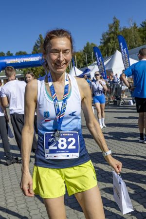 Uśmiechnięta biegaczka w neonowych spodenkach z numerem 282 z medalem i białą torbą w strefie finiszu.