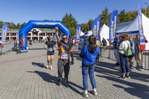 Biegacz z numerem 205 unosi pięść w geście zwycięstwa, kobieta w niebieskiej bluzie fotografuje go telefonem.