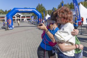 Kobieta w białej bluzie mocno obejmuje biegaczkę w niebieskiej koszulce tuż przy bramie finiszowej.