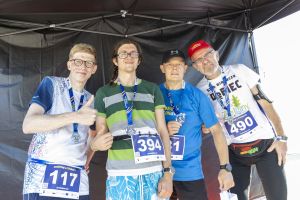 Czterech mężczyzn z medalami pozuje pod czarnym namiotem; widoczne numery startowe 117, 394, 81 i 490.