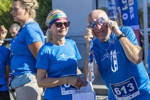 Biegacz z numerem 613 trzyma dwa medale przy oczach jak gogle; obok uśmiechnięta uczestniczka w tęczowej opasce.