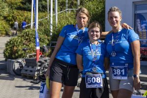 Trzy kobiety w niebieskich koszulkach z medalami; numery 508 i 381, jedna trzyma banana i białą torbę.
