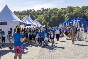Strefa imprezy z rzędem białych namiotów, tłumem w niebieskich koszulkach i niebieską bramą mety w oddali.