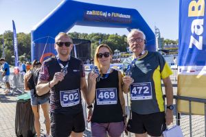 Troje finisherów z medalami i numerami 502, 469 oraz 472 przed niebieską bramą finiszu zaBIEGaj o FUNdusze.