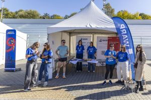 Stoisko WARP pod białym namiotem z koszulkami Pewny Start; uczestnik z numerem 333, kobieta z małym psem.