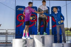 Laureaci na podium: zwycięzca z dyplomem, biegacz z napisem Baranowice Biegają wymienia uścisk z trzecim miejscem.