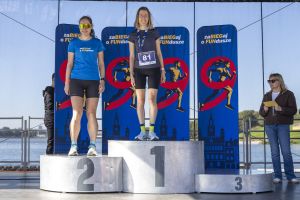 Podium kobiet: zwyciężczyni z numerem 81 w szarej koszulce i druga w niebieskiej koszulce biegu; trzeci stopień pusty.