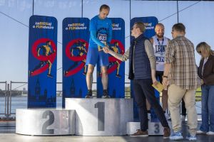 Zwycięzca z numerem 623 wymienia uścisk dłoni z urzędnikiem na podium; trzeci z numerem 376 i medalem stoi obok.