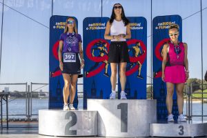 Trzy kobiety na pełnym podium z medalami; środkowa w białym topie, po bokach numer 397 i różowy strój biegowy.